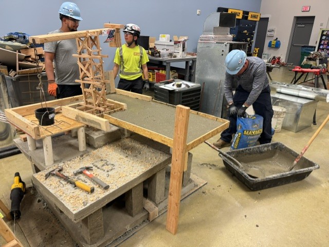 Participants practicing hands-on construction fundamentals with concrete and framing materials in a workshop